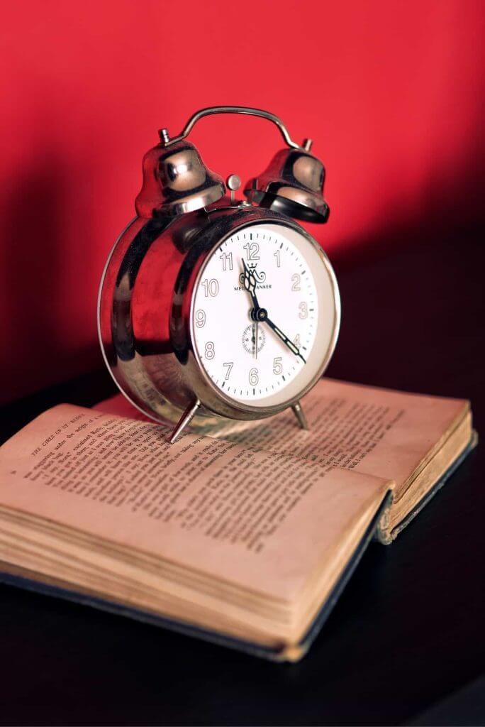 An alarm clock placed on an old book with red backlighting.