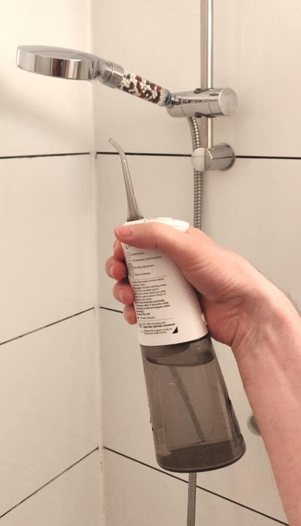 A male arm holding an oral douche beneath a showerhead.