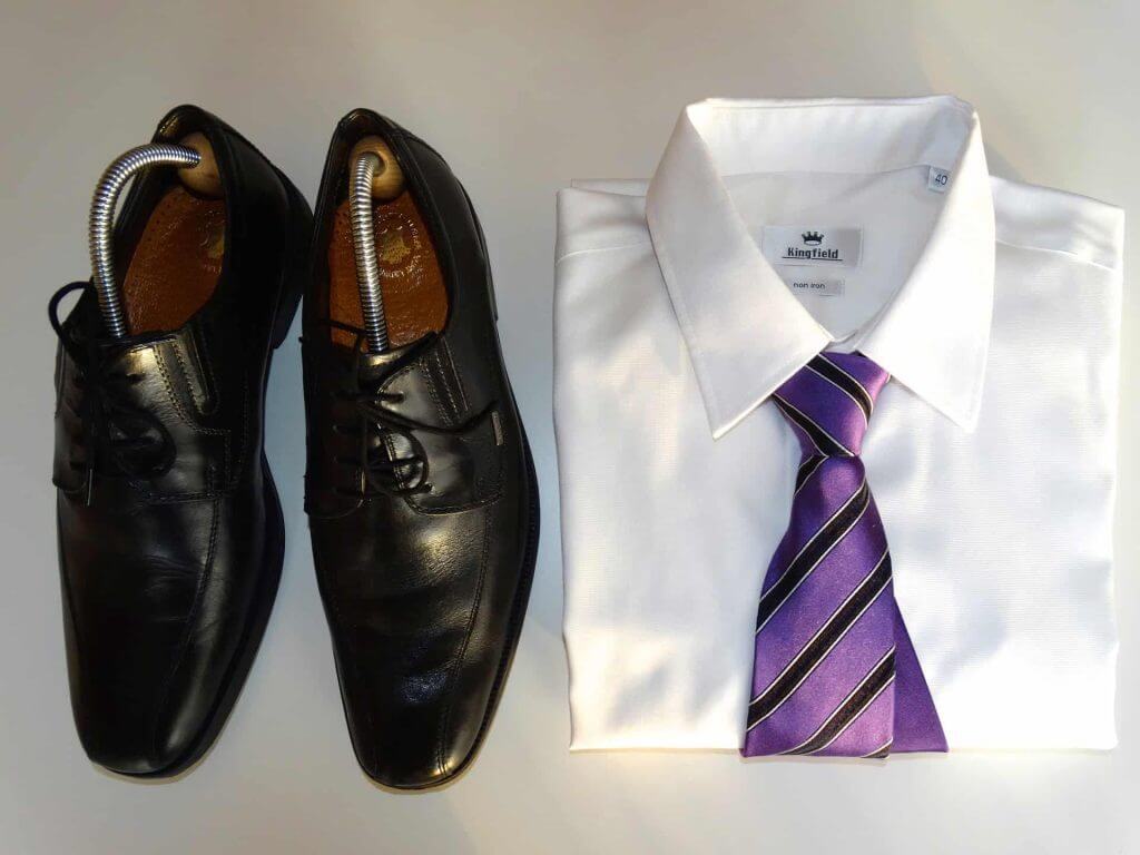 A pair of black shoes with stretchers, and a white shirt with a knotted, purple striped tie.