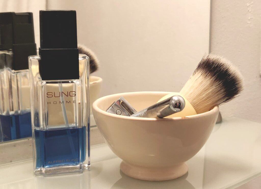 A shaving bowl with brush and safety razor, and a bottle of Alfred Sung Homme cologne