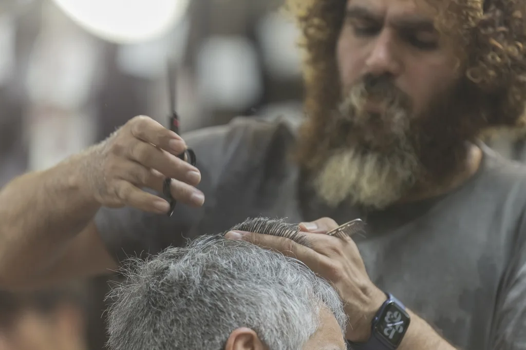 A barber trimming the hair of a man with gray hair.