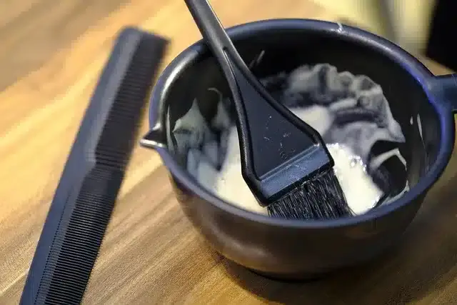 A black bowl with hair dye and a tinting bush, beside it a comb