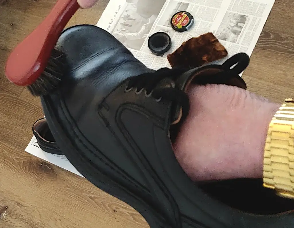 A man applying shoe polish to a black pair of shoes using a brush.