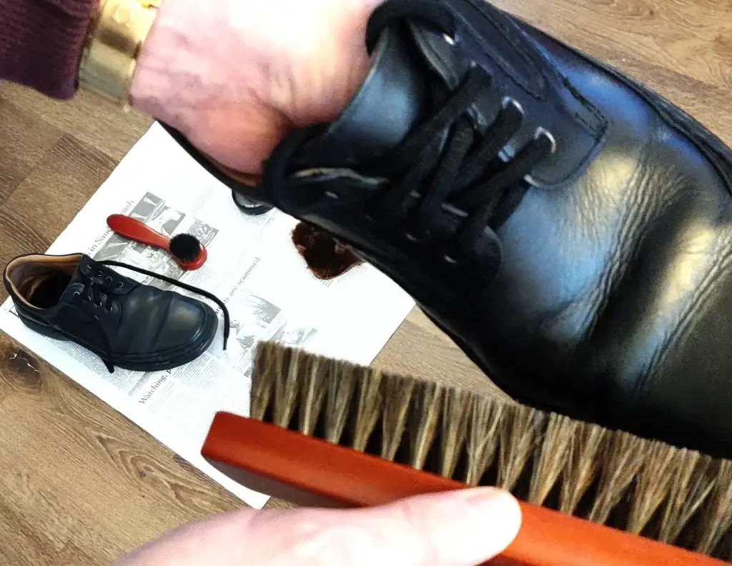 Man shining a black shoe with a horsehair buffing brush.