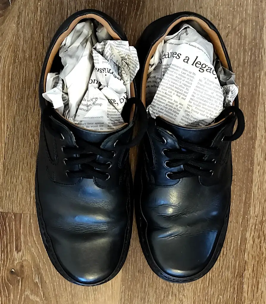 A pair of black shoes stuffed with newspaper, either because they are wet or in storage.