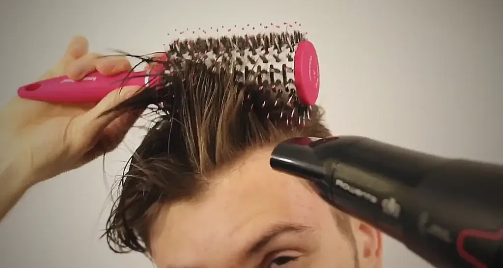 Man using a round brush while blow-drying his hair