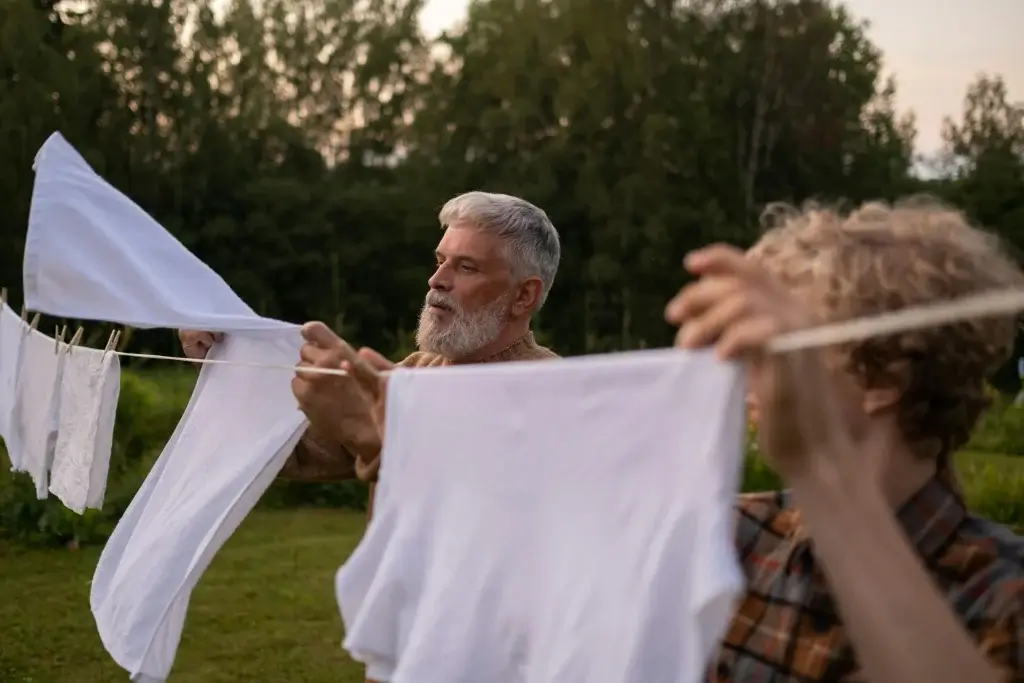 An older man teaching a beginner to laundry how to hang wet washing out on a line.