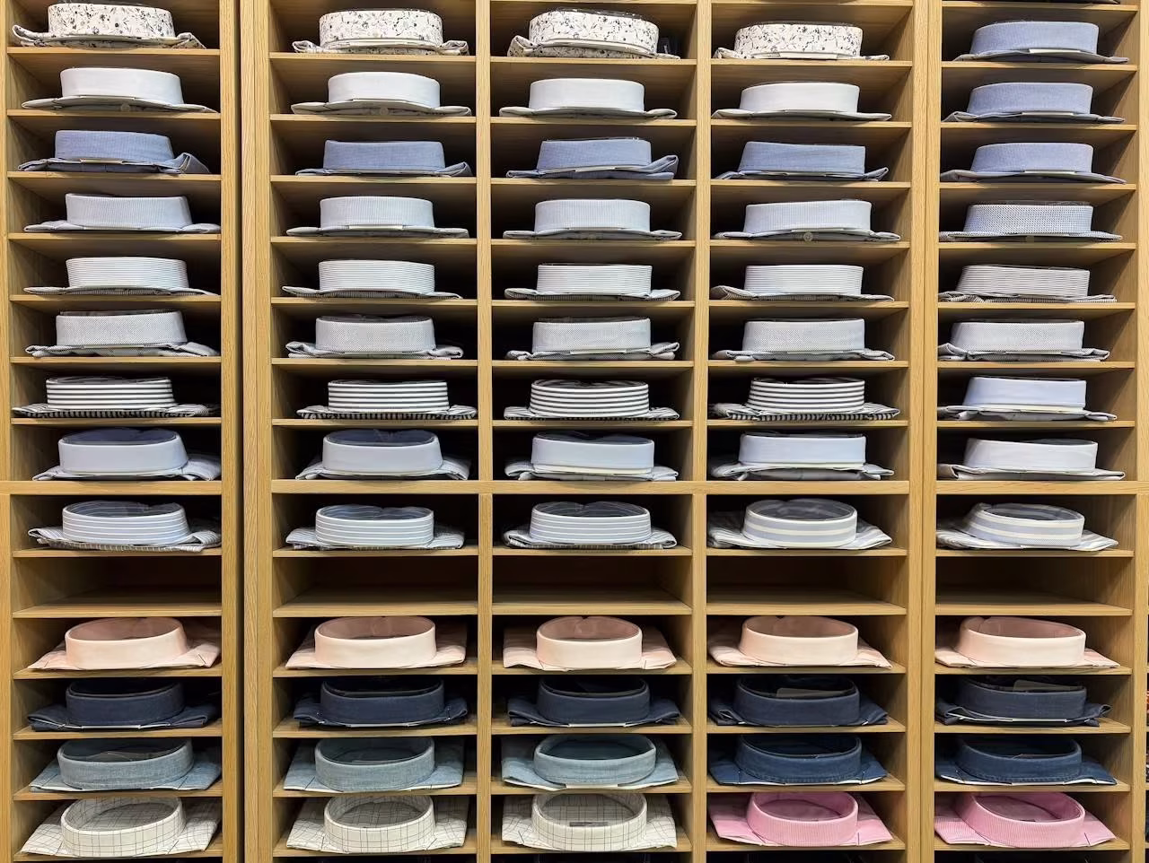 A wooden shelving unit displaying neatly folded dress shirts in various colors and patterns, highlighting the diversity of dress shirt colors for professional wear.