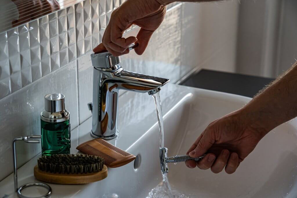 A man carrying out his daily grooming routine at a sink, rinsing his safety razor.