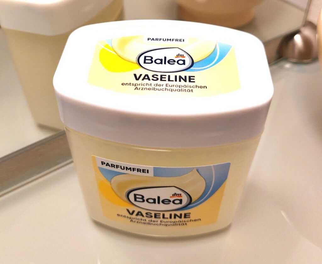 Jar of petroleum jelly, a man's skincare staple, on a bathroom shelf before a mirror.