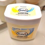 Jar of petroleum jelly, a man's skincare staple, on a bathroom shelf before a mirror.