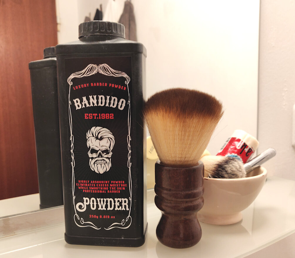 Barber powder container labeled “Bandido Powder” alongside a neck duster and shaving kit on a bathroom counter.