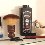 A curated display of classic grooming tools, including barber powder, a neck duster, a shaving kit in a ceramic bowl, a beard brush, a mustache comb, hairdressing scissors, and a bottle of cologne—evoking traditional barbershop rituals and refined masculine care.