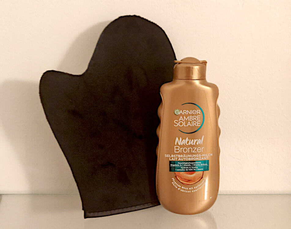 Garnier Ambre Solaire Natural Bronzer self-tanning lotion with a black mitt—used to apply self-tanner evenly for streak-free, professional-looking results.