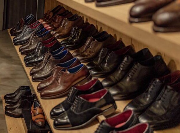 A neatly arranged display of men’s leather shoes on wooden shelves, all brand new, all in need of breaking in.