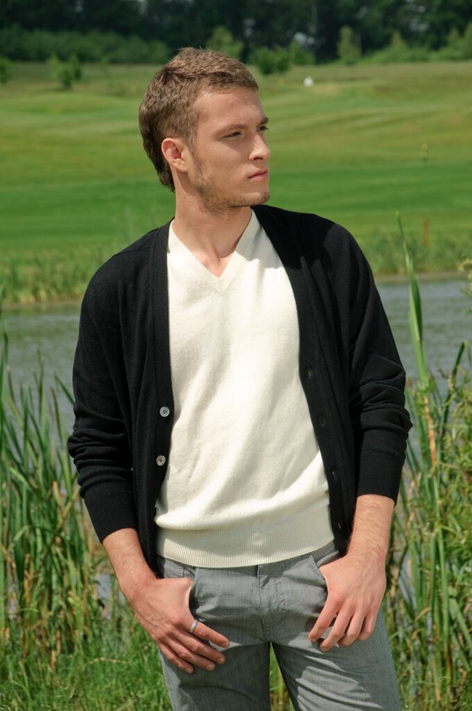 A man wearing a black V-neck cardigan over a cream V-neck sweater.