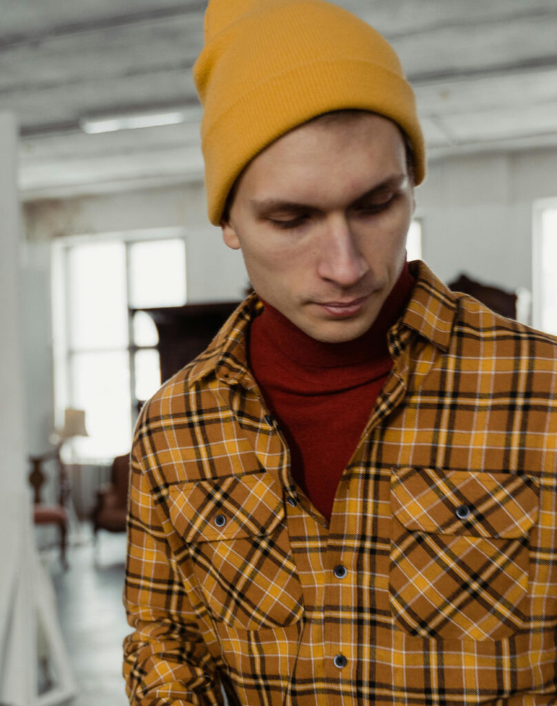 A man wearing a warm beanie and layered clothing indoors, illustrating what to wear in a cold house.