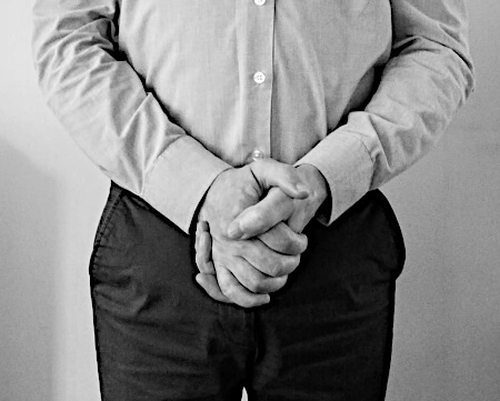 Man with his hands clasped in front of him at navel height.