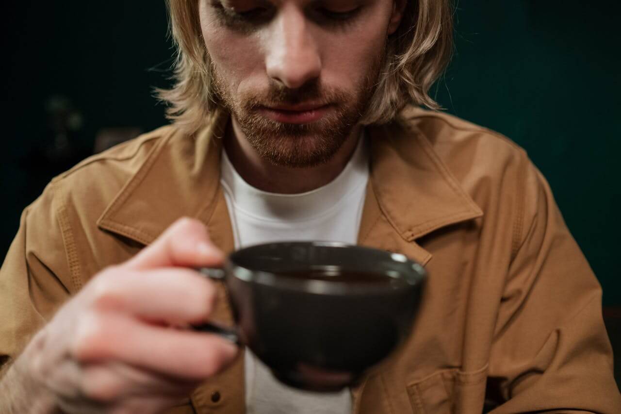 A man who is trying to reduce caffeine consumption looking thoughtfully at a cup of coffee.