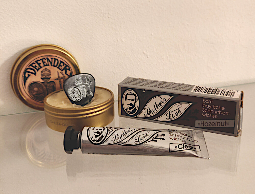 Open Defender tin with a guitar pick stuck into the balm, shown alongside Brother’s Love Bavarian mustache wax products to illustrate what men compare when choosing beard balm or mustache wax.