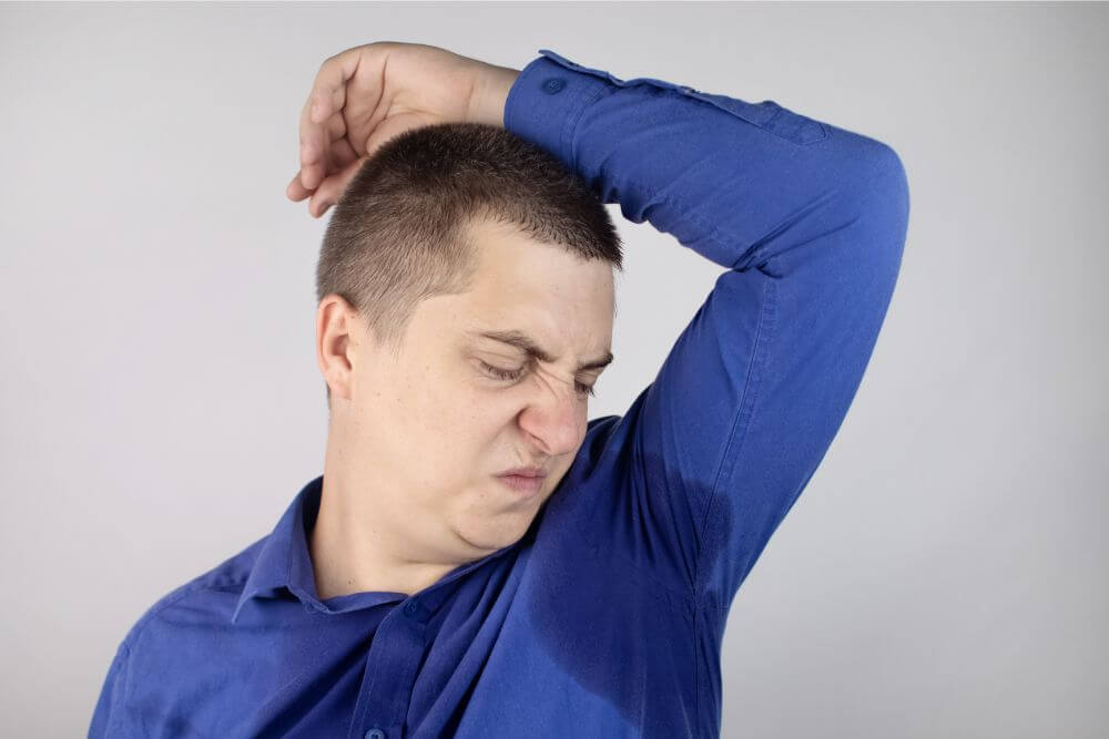 Man smelling his sweaty armpit while wrinkling his nose.