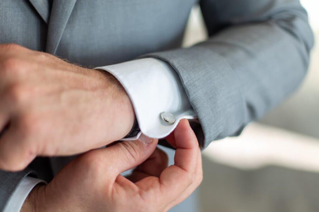 A man adjusting mother-of-pearl cufflinks.