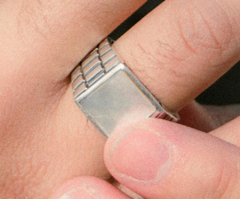 A close-up of a plain signet ring being adjusted on a man’s finger.