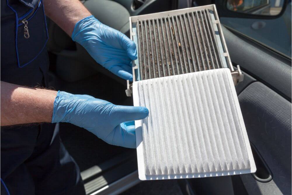 A man wearing blue nitrile gloves while holding a used and a new car cabin filter.