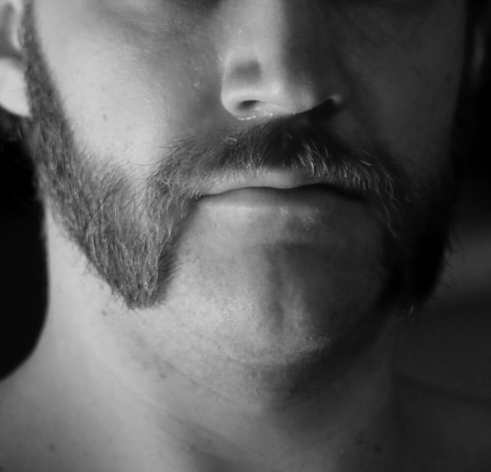 Black‑and‑white close‑up of a man’s lower face showing a friendly mutton chops beard style.