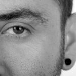 A half facial image of a man wearing a low gauge flesh tunnel rendered in black and white.