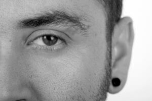 A half facial image of a man wearing a low gauge flesh tunnel rendered in black and white.