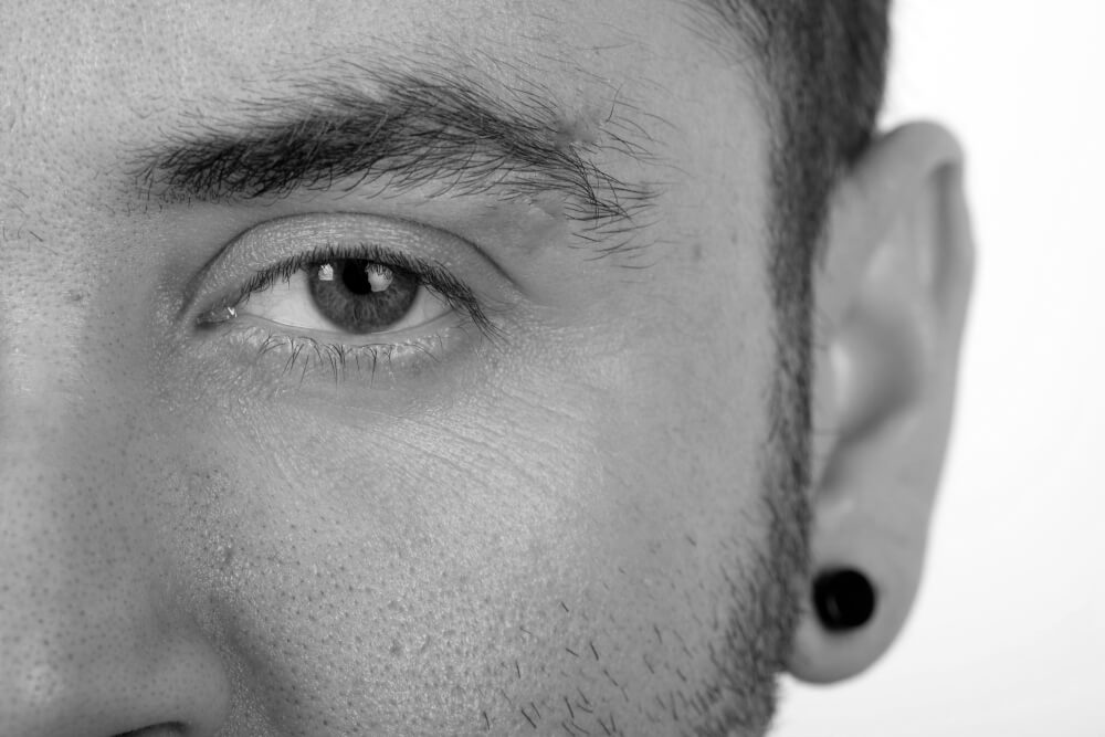 A half facial image of a man wearing a low gauge flesh tunnel rendered in black and white.