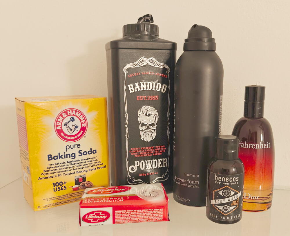 A selection of products for men’s grooming and hygiene, including baking soda, Lifebuoy soap, Bandido powder, Homme shower foam, Benecos body wash, and a Fahrenheit fragrance arranged on a shelf.