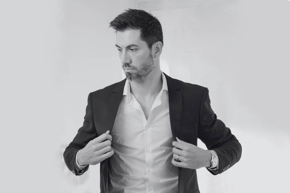 A man slipping a suit coat over a dress shirt that has a perfectly symmetrical collar and placket.
