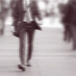 A man in a suit walking briskly along a city street, with motion blur suggesting a long exposure.