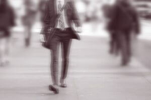 A man in a suit walking briskly along a city street, with motion blur suggesting a long exposure.