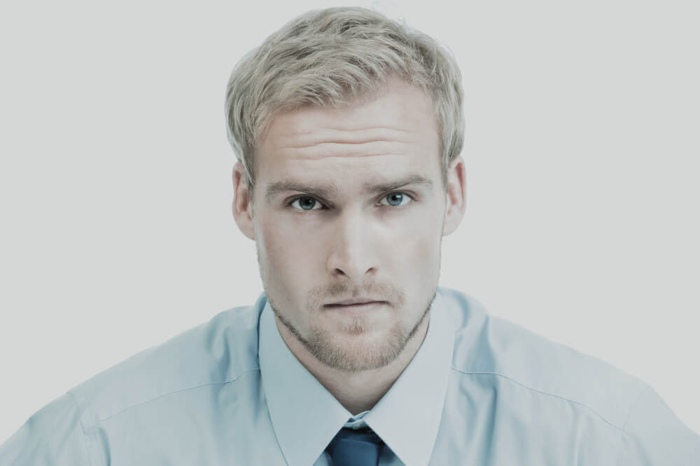 A pale blond man wearing a light blue shirt and dark blue tie.