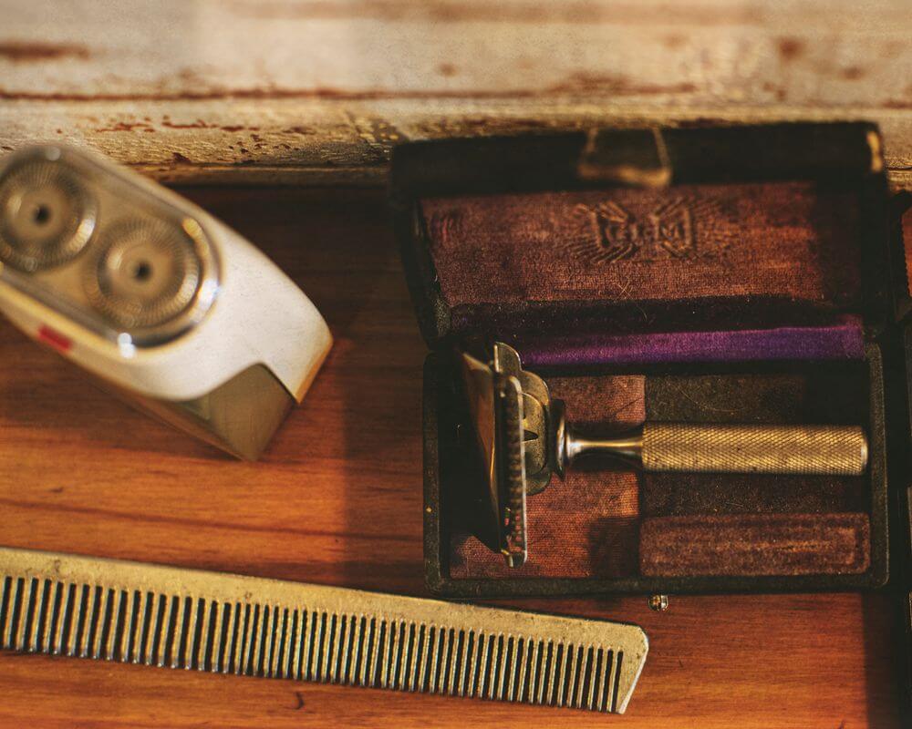 A vintage two-head rotary electric shaver, a vintage safety razor, and a metal comb.